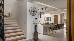 A modern kitchen with a central island, a dining area with chairs, and a staircase with wooden steps. - Villa Lumi Zadar Villas (Murvica)