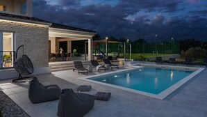 An outdoor swimming pool area with lounge chairs and a hanging chair, surrounded by a stone wall and a covered patio. - Villa Lumi Zadar Villas (Murvica)