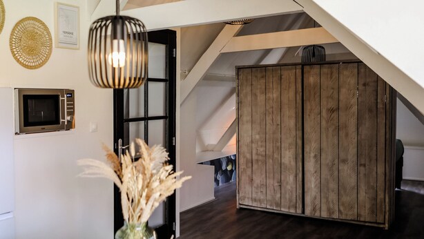 A modern kitchen with a microwave, a hanging pendant light, and a wooden cabinet. - Cozy apartment in center of Yerseke (Yerseke)