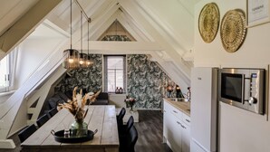 A modern kitchen with a dining area, featuring a wooden table, black chairs, and a hanging light fixture. - Cozy apartment in center of Yerseke (Yerseke)