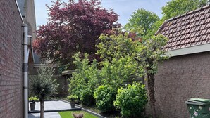 A patio area with a wooden table and chairs, surrounded by brick walls and greenery. - Cozy apartment in center of Yerseke (Yerseke)