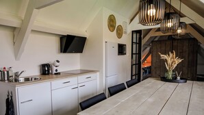 A modern kitchen with white cabinets, a wooden countertop, and a dining table with chairs. There are hanging pendant lights and a flat-screen TV mounted above the counter. - Cozy apartment in center of Yerseke (Yerseke)