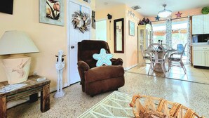 A living room with a brown armchair, a small table with a lamp, a wicker chair, and a starfish decoration. - Charming 2-bedroom house in beautiful Port Charlotte with Pool, Hot tub, & WiFi (Port Charlotte)