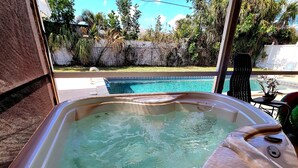 A hot tub with a view of a swimming pool and surrounding greenery. - Charming 2-bedroom house in beautiful Port Charlotte with Pool, Hot tub, & WiFi (Port Charlotte)