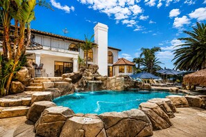 A pool with a waterfall, surrounded by rocks and palm trees, with a building in the background. - 20% Off July 14&15! Great 4 Families Pool, Jacuzzi (Temecula)