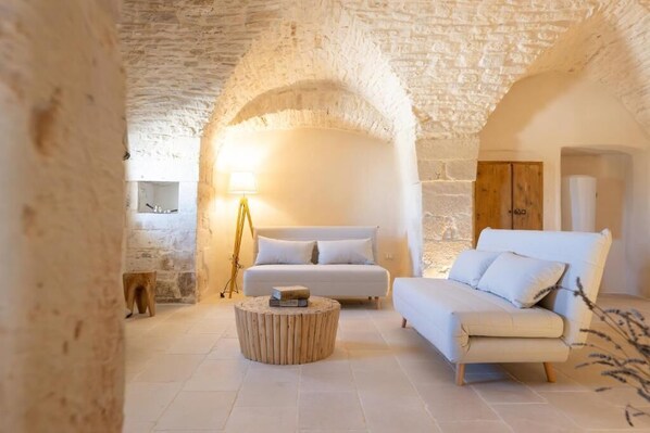 A cozy room with a stone ceiling, a white sofa, a round wooden coffee table, and a lamp.