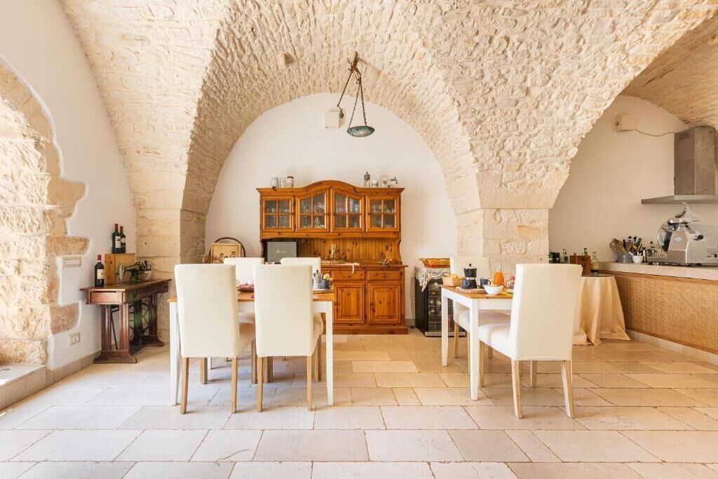 Un comedor rústico con techo de piedra, armarios de madera y sillas blancas.