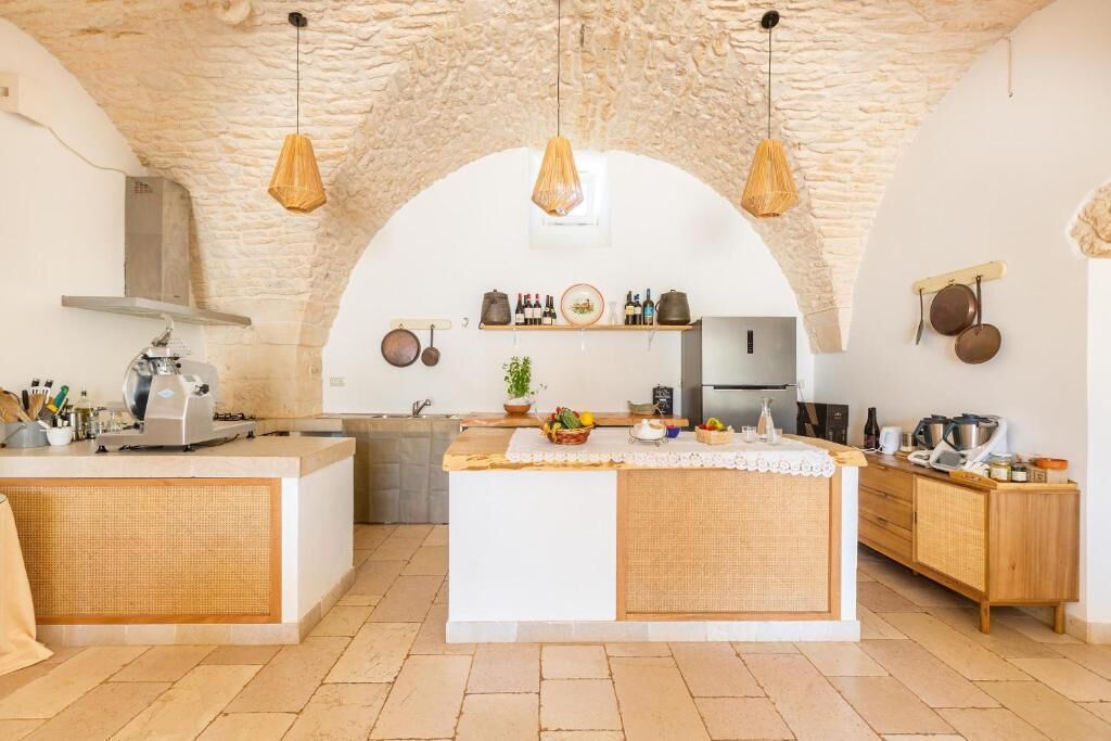 A kitchen with a central island, stone arch ceiling, hanging pendant lights, and wooden cabinetry.