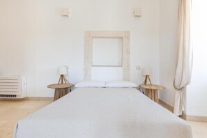 Un dormitorio minimalista con una cama grande, dos mesitas de noche con lámparas, un radiador y una ventana con cortinas.