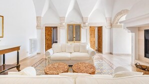 A spacious living room with a white sofa, two round coffee tables, and a fireplace.