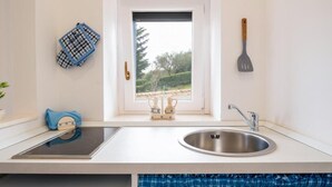 A modern kitchen with a stainless steel sink, a window with a view of greenery, and a spatula hanging on the wall. - The Villa Resort, sleeps 2 + shared pool (MARTINA FRANCA)