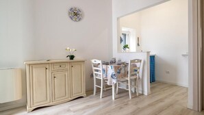 A dining area with a table set for two, a cream-colored cabinet, and a wall-mounted clock. - The Villa Resort, sleeps 2 + shared pool (MARTINA FRANCA)