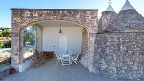 A stone archway leading to a patio with a table and chairs, a door, and a pool in the background. - The Villa Resort, sleeps 8 + shared pool (MARTINA FRANCA)