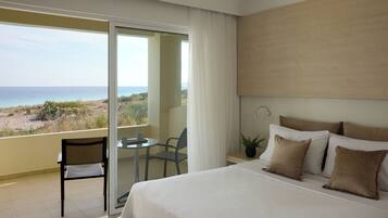 A hotel room with a bed, a chair, a small table, and a view of the beach.