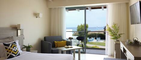 Habitación de hotel moderna con una cama grande, un sofá, una mesita y un balcón con vistas al mar.