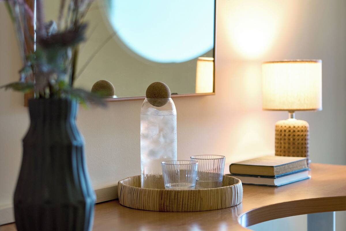 A wooden desk with a vase of dried plants, a glass jar with a lid, and a lamp on a bedside table.