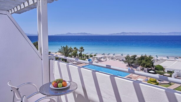 A balcony with a clear view of a swimming pool, beach umbrellas, and palm trees. - Blue Bay Beach Resort (Rhodes)