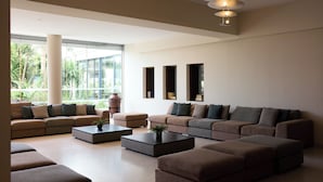 A spacious living area with multiple sofas and ottomans, a coffee table, and a large window providing a view of greenery outside. - Blue Bay Beach Resort (Rhodes)