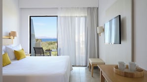 A hotel room with a large bed, a desk, a chair, a TV, and a balcony with a view of the sea. - Blue Bay Beach Resort (Rhodes)