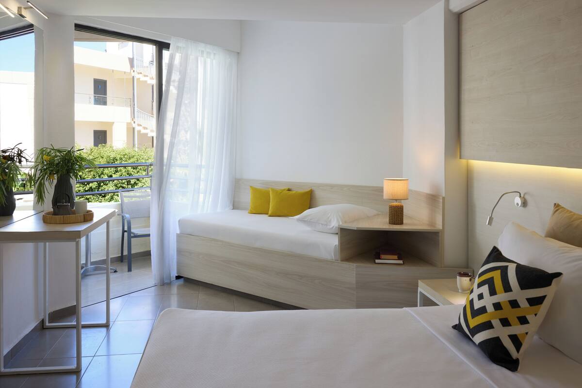 A modern hotel room with a bed, bedside table, and a view of the outside balcony.