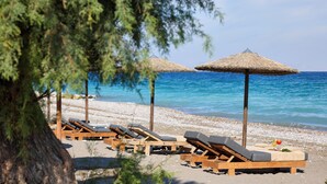 A beach with wooden lounge chairs and thatched umbrellas, a tree, and a clear blue sea. - Blue Bay Beach Resort (Rhodes)