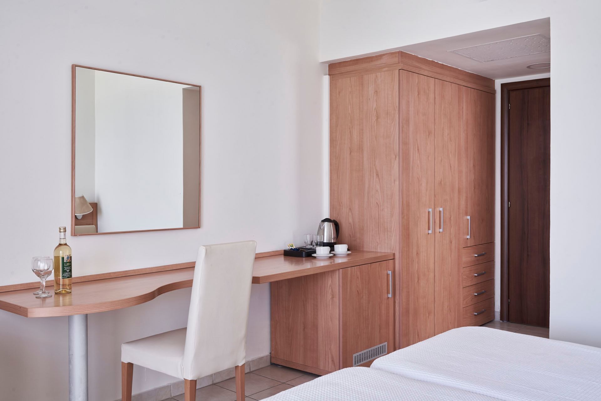Habitación de hotel con escritorio de madera, una silla, cama, armario y espejo.
