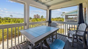 A covered outdoor deck with a table and chairs, overlooking a beach and distant buildings. - Lost Key Villas Golf & Beach Club ~Stillwater -  NO HASSLE CHECK OUT (Perdido Key)