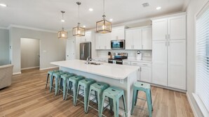 A modern kitchen with white cabinets, a central island with bar stools, stainless steel appliances, and pendant lighting. - Lost Key Villas Golf & Beach Club ~Stillwater -  NO HASSLE CHECK OUT (Perdido Key)