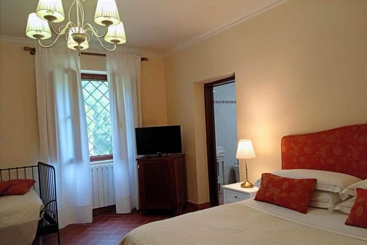 Et hotelværelse med seng, fjernsyn, lampe og stol.