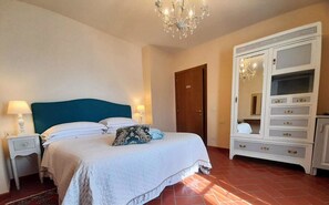 Ein Schlafzimmer mit einem Bett, Nachttischen, einer Kommode, einer Deckenleuchte und einer Tür.