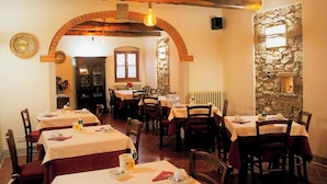Un comedor con mesas dispuestas para comer, una pared de piedra y un techo de madera rústica.