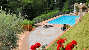 Una piscina con cubierta de piedra, rodeada de una valla y follaje.