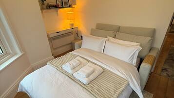 Une chambre à coucher comprenant un lit, des tables de chevet, une commode, une lampe, une étagère avec des livres et des objets décoratifs, et une fenêtre.