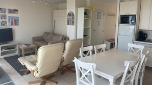 A living room with a sofa, chairs, a TV, and a dining table. - Penthouse in Koksijde With Stunning Sea View (Nieuwpoort)