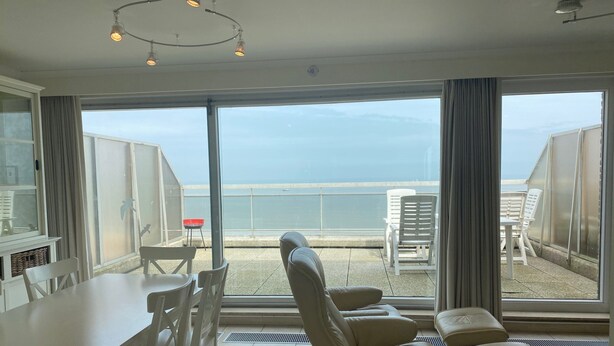 A balcony with a view of the sea, a dining table with chairs, and a sofa with cushions. - Penthouse in Koksijde With Stunning Sea View (Nieuwpoort)