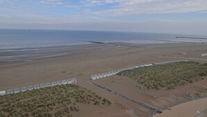 A beach with a long pier extending into the sea, a sandy area with small structures, and sparse vegetation. - Penthouse in Koksijde With Stunning Sea View (Nieuwpoort)