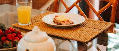 Une table de petit-déjeuner avec un verre de jus d’orange, une assiette contenant une part de gâteau, une théière et un bol de fraises.