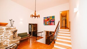 Un'ampia zona giorno con camino in pietra, un divano verde, una scala in legno e un quadro astratto dai colori vivaci appeso al muro.
