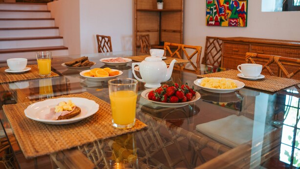Una colazione servita su un tavolo di vetro, con sedie in vimini e diversi cibi tra cui succo d'arancia, fragole e uova strapazzate.
