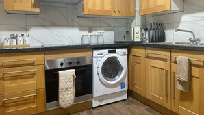 Una cocina con armarios de madera, una campana extractora de acero inoxidable, una lavadora integrada y un lavabo con grifo.