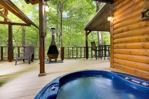 A wooden cabin with a hot tub, outdoor seating, and a wood stove.