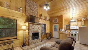 Een gezellig interieur van een chalet, met een stenen open haard, een bank, een eethoek en een keuken met een magnetron.