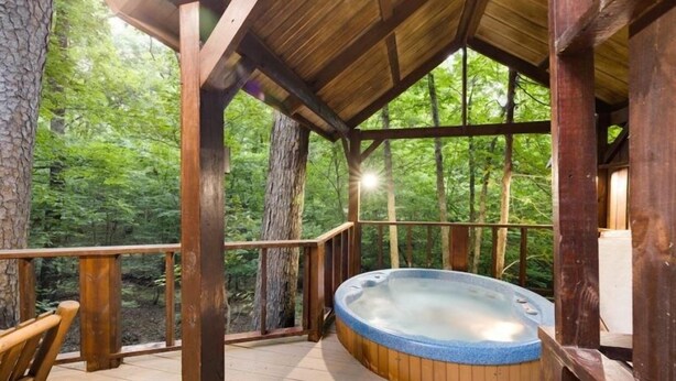 Een hottub in een houten tuinhuis met uitzicht op een bos.