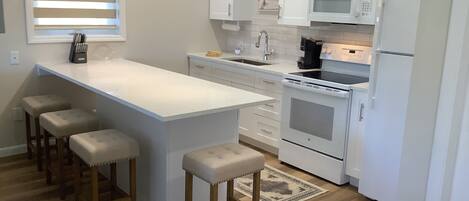 A modern kitchen with white cabinetry, a central island with stools, a microwave, an oven, and a sink.