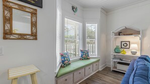 A room with a built-in bench, a white sofa, a small table, and a wall-mounted shelf with decorative items. - Seagrove Beach - Private Pool - Pet Friendly (Santa Rosa Beach)
