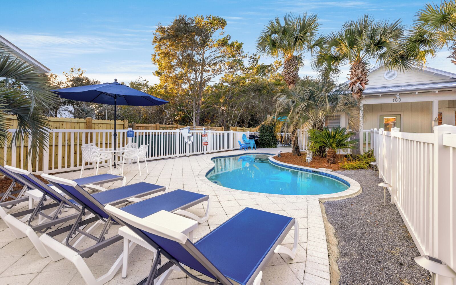 A pool area with lounge chairs, a blue umbrella, and a fenced deck.