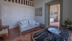 A room with a sofa, a dining table with a plate, a chair, and a bed in the background. - Historic villa with swimming pool surrounded by nature (Umbria)