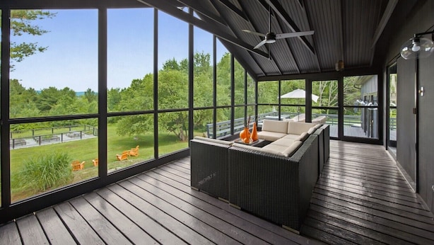 A covered outdoor seating area with a sofa and chairs, large windows, and a ceiling fan.
