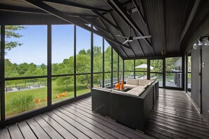 Un área de estar al aire libre techada con sofá y sillas, ventanas amplias y ventilador de techo.