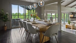 A modern dining area with a large table, grey chairs, and pendant lights.